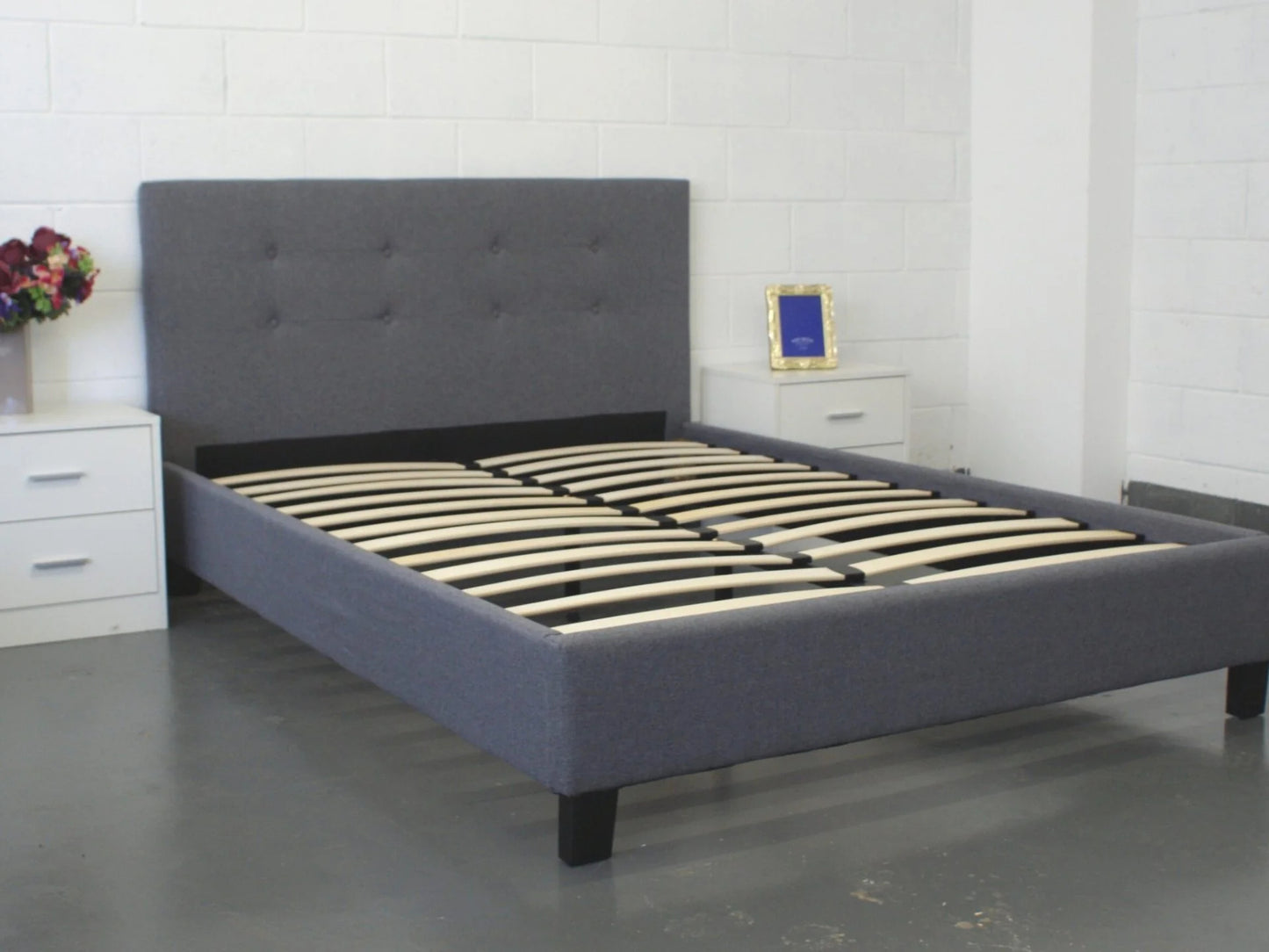 Gray upholstered bed with wooden slats in a room setting.
