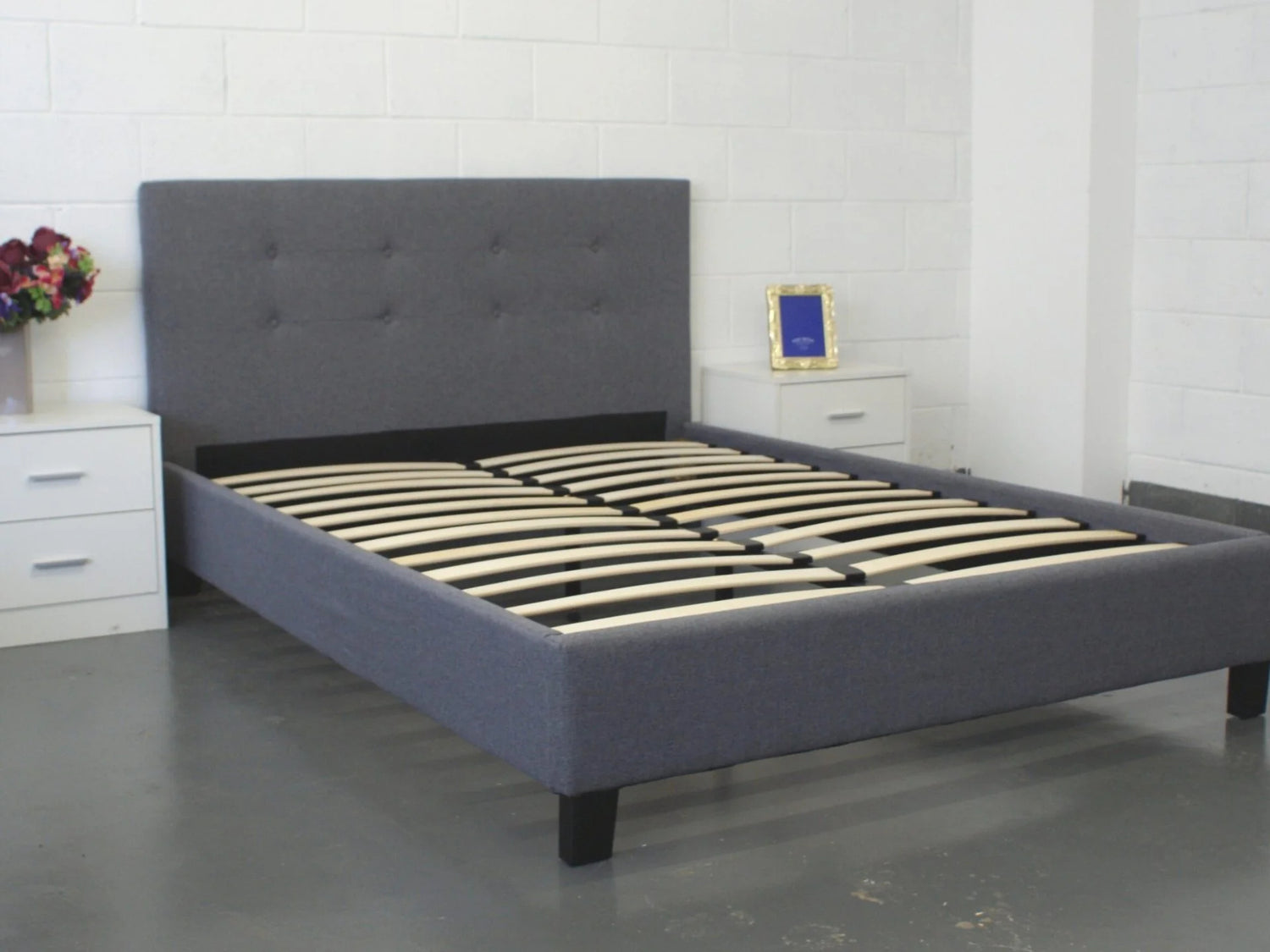Gray upholstered bed with wooden slats in a room setting.