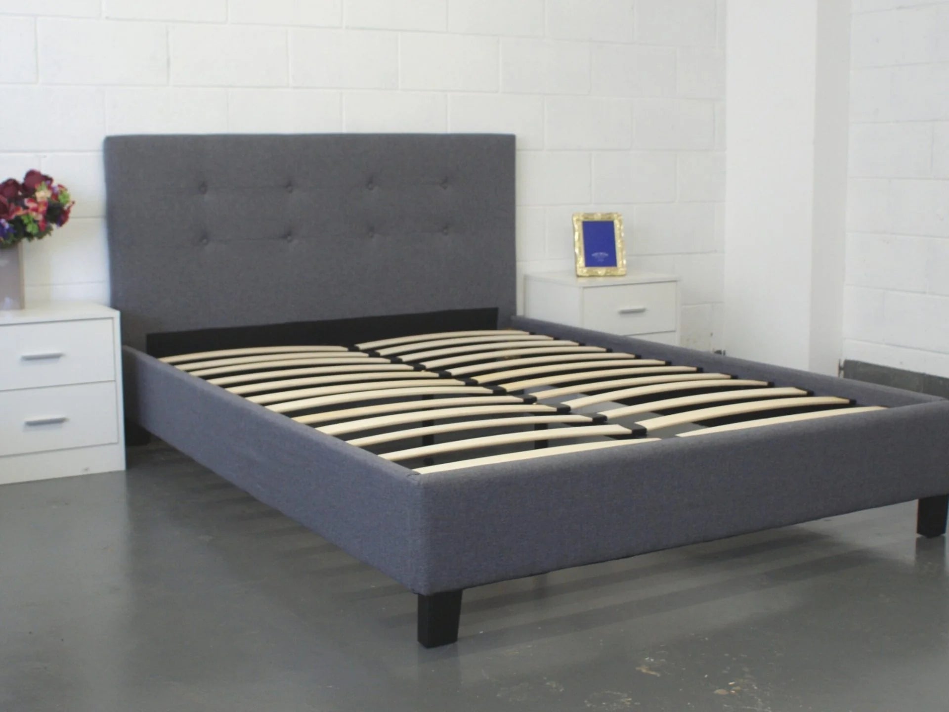 Gray upholstered bed with wooden slats in a room setting.