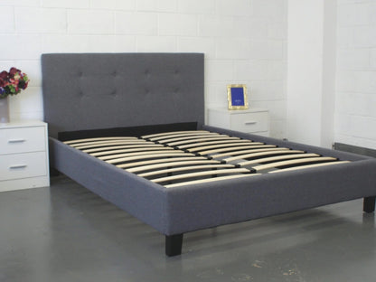 Gray upholstered bed with wooden slats in a room setting.
