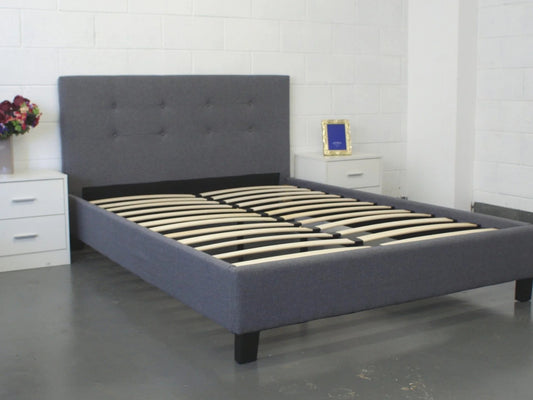 Gray upholstered bed with wooden slats in a room setting.